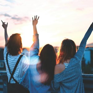 Trzy osoby z uniesionymi rękami o zachodzie